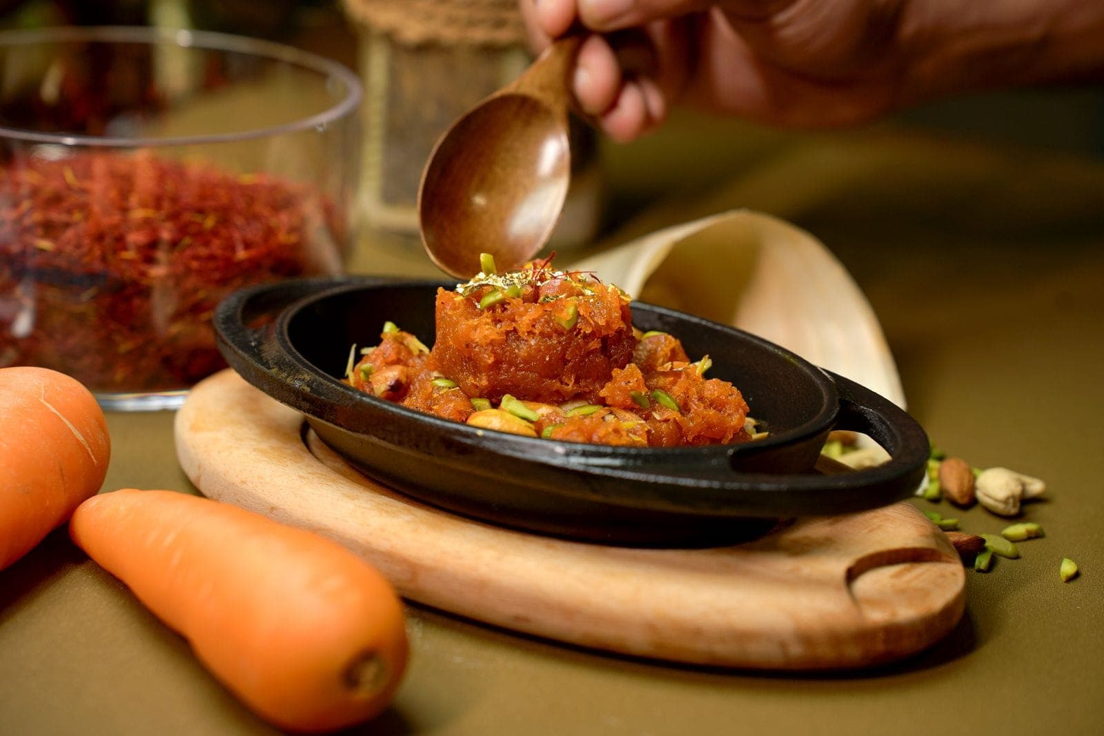 Gajar halwa topped with pistachios and gold leaf in a black iron dish