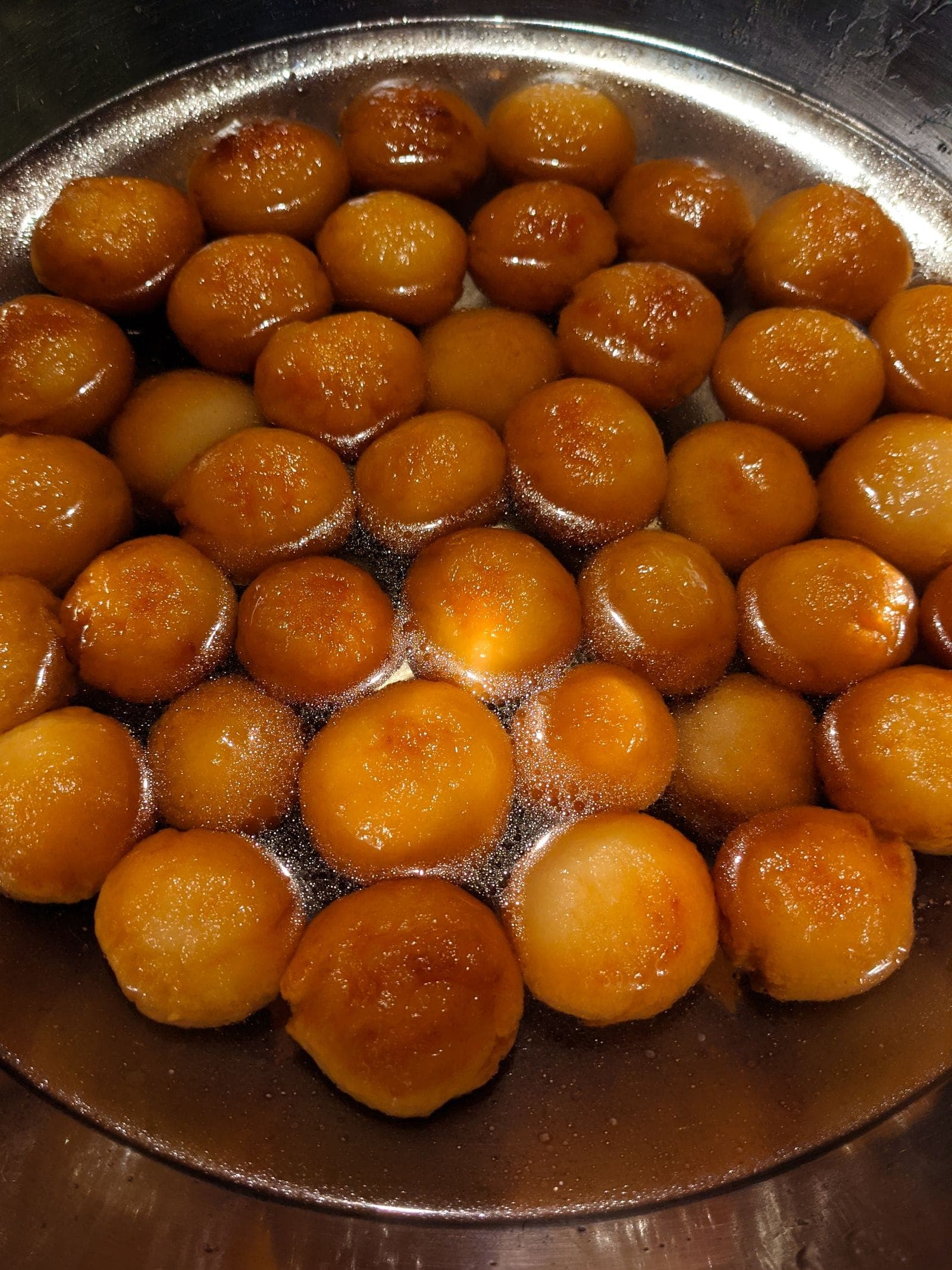 Gulab jamun glistening in syrup in a steel dish