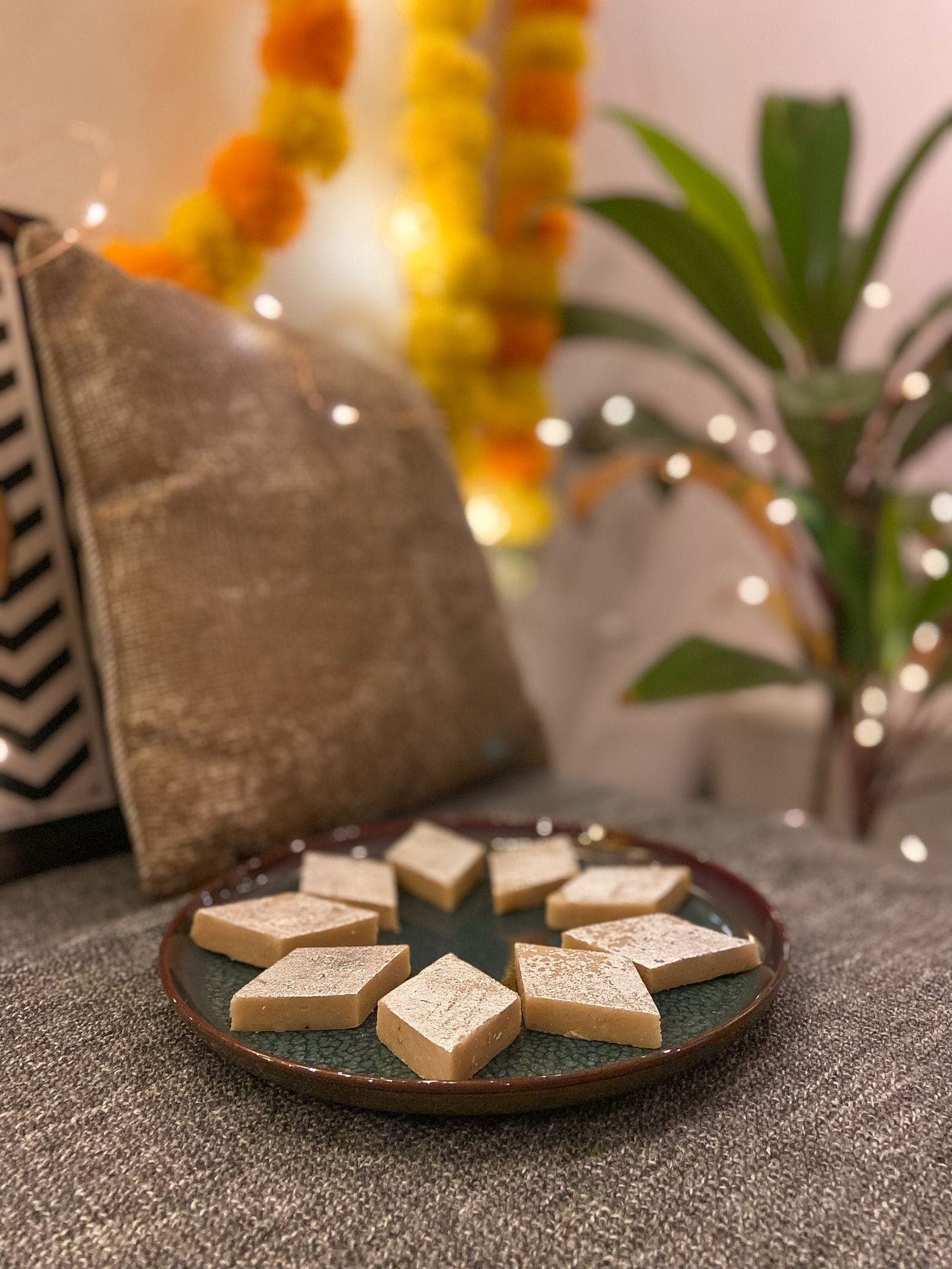 Diamond-cut kaju katli pieces with silver leaf on a dark plate