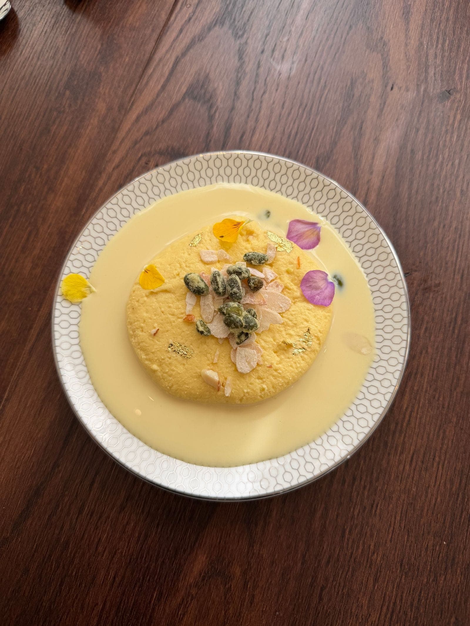 A rasmalai disc in saffron milk topped with pistachios and almond flakes