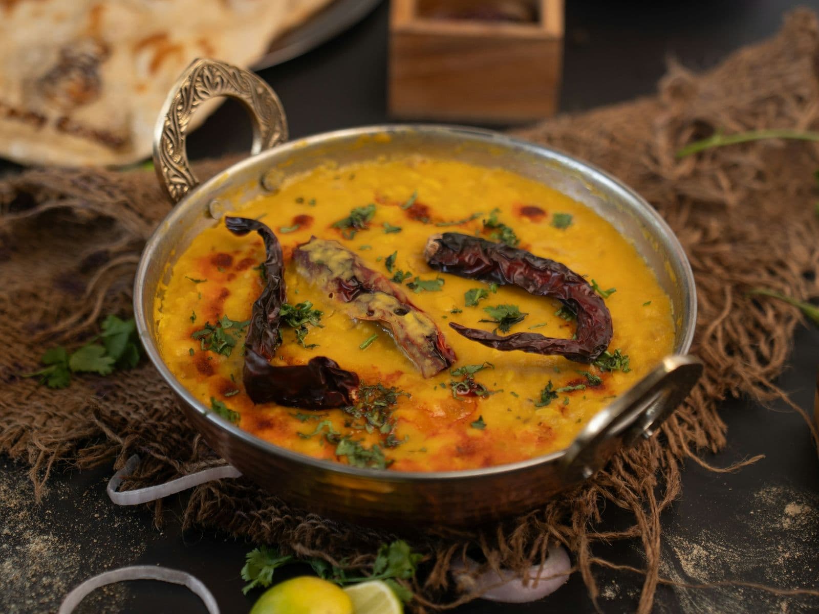 A bowl of yellow dal with dried red chillies and coriander, with bread behind it